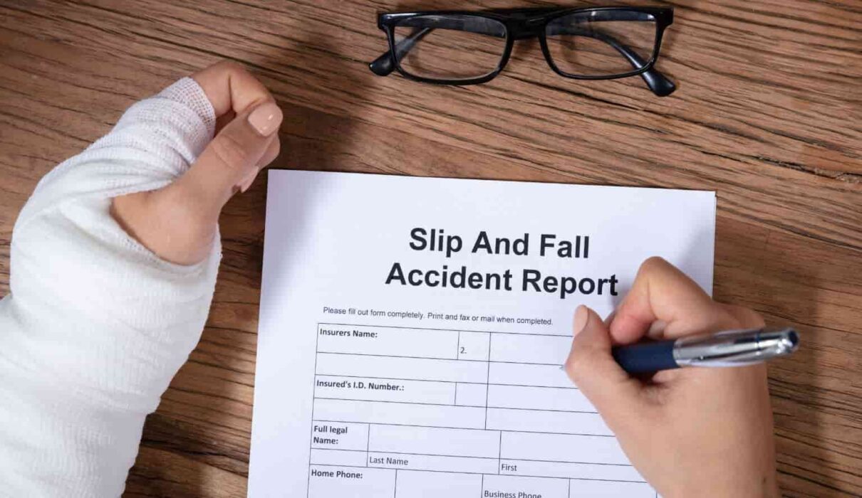 A person lying on the floor after a hazardous fall in a public building while a caution sign stands nearby, illustrating a Slip and Fall Lawsuit involving unsafe property conditions and injury claims.