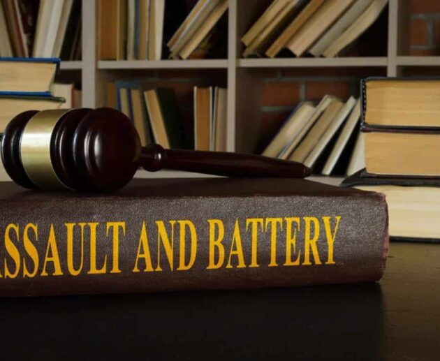A courtroom-themed illustration representing Assault and Battery, showing a victim with visible injuries speaking to a lawyer while legal documents, a gavel, and scales of justice symbolize a civil and criminal legal case.