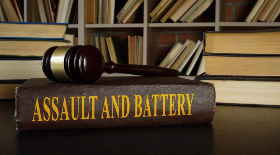 A courtroom-themed illustration representing Assault and Battery, showing a victim with visible injuries speaking to a lawyer while legal documents, a gavel, and scales of justice symbolize a civil and criminal legal case.