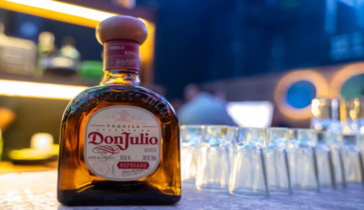 A bottle of premium tequila on a wooden counter with legal documents in the background.