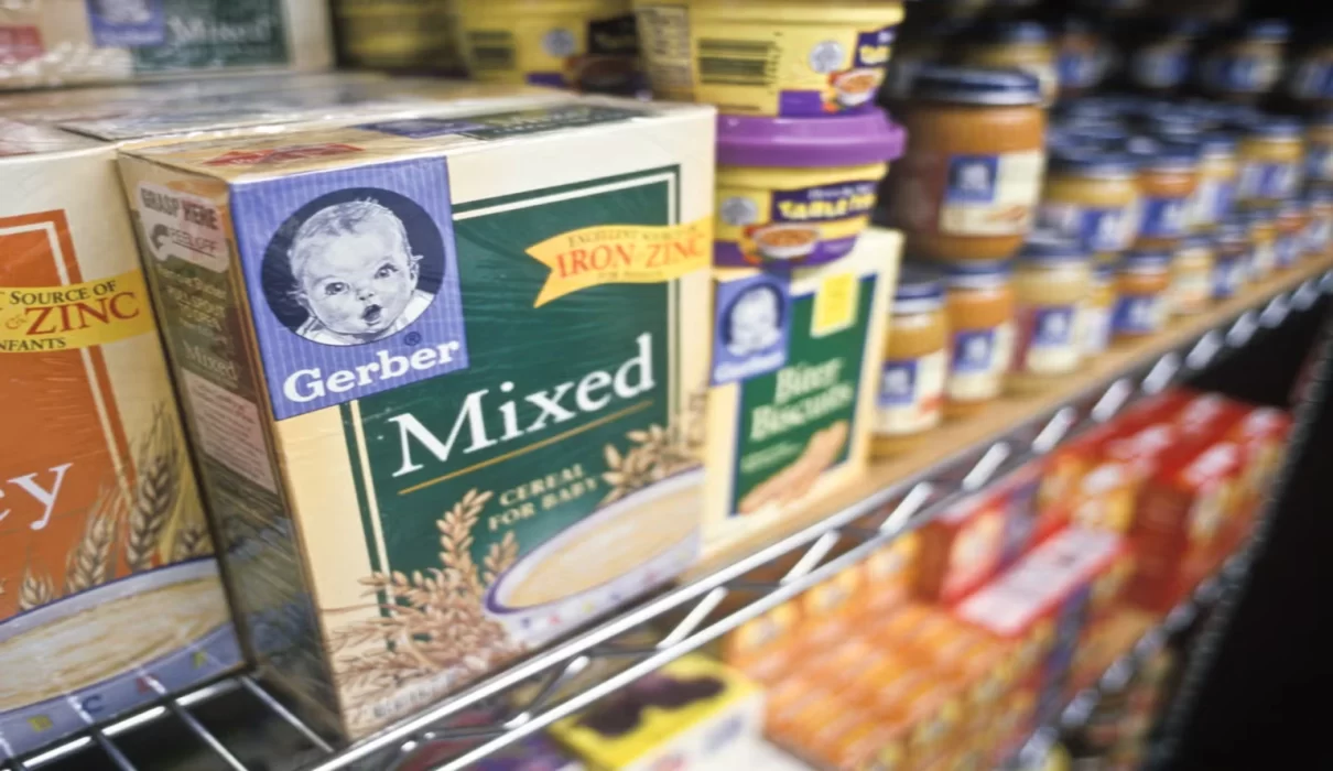 Illustration of a magnifying glass over a batch code on a baby snack box beside a recall alert icon