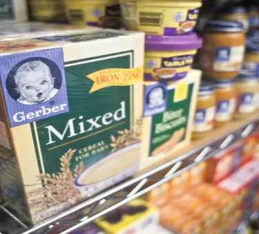 Illustration of a magnifying glass over a batch code on a baby snack box beside a recall alert icon